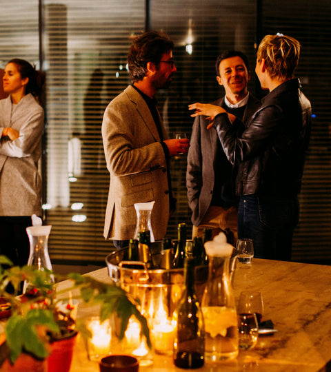 A group of five people gathered in dim lighting, having discussions in front of a table full of drink options