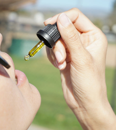 A woman in sun glasses dropping some drops of CBD oil in her mouth. 