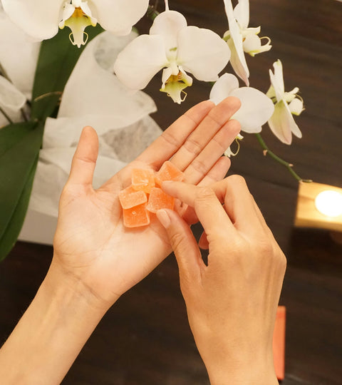 A pair of hands holding several CBD gummies next to a white orchid plant, against a dark wood background